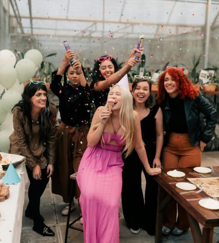 Group of women enjoying a festive birthday party with confetti indoors.