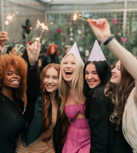 Group of young women celebrating with party hats and sparklers indoors, capturing lively birthday moments.
