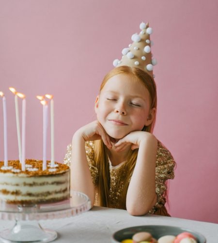 A young girl celebrating her birthday with a cake, wearing a festive party hat.